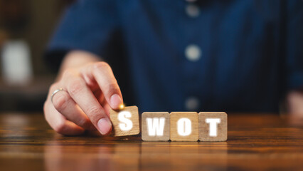 Person building wooden blocks to spell 'SWOT'